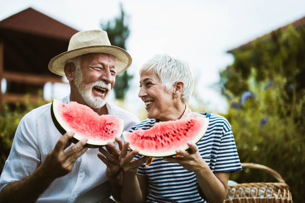 Cheerful mature couple having fun while eating watermelon during picnic day in nature.